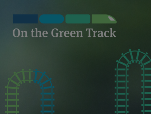 Grafika kampanje On the green track - zeleno modre tračnice z zeleno modrim vlakom, pod njim napisano ime kampanje
